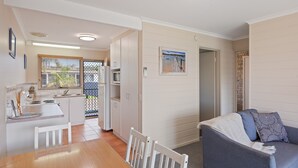 A compact living space with a kitchenette, a dining area, and a seating area with a couch. - Fishpen Views - Merimbula (Merimbula)