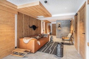 A modern interior with a wooden reception desk, a sofa with fur throw, a chair, and a metal bucket. - Peridot – Family alpine escape, Champagny (Champagny-en-Vanoise)