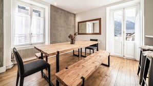 A modern dining area with a wooden table, chairs, and benches. There is a large mirror on the wall and a view of mountains through the windows. - Brina – Chamonix Apartment with Mont Blanc View (Chamonix-Mont-Blanc)