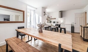 Une cuisine moderne avec des meubles blancs, une hotte en acier inoxydable et un coin repas comprenant une table et des bancs en bois.