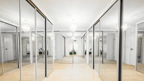 A hallway with mirrored walls and a chandelier, leading to a room with a bed and a green chair. - Huge Digbeth Apt, Sleeps 8, 5bed, Free Parking. (Birmingham)