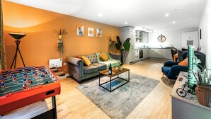 A living room with a foosball table, a sofa, a coffee table, and a kitchen in the background. - Huge Digbeth Apt, Sleeps 8, 5bed, Free Parking. (Birmingham)