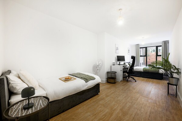 A bedroom with a bed, bedside table, desk, chair, and a potted plant. - Huge Digbeth Apt, Sleeps 8, 5bed, Free Parking. (Birmingham)
