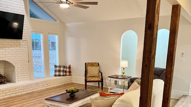 A living room with a fireplace, a brown leather sofa, a white armchair, and a wooden coffee table. There is a television mounted on the wall and a ceiling fan. - The Star Point Lakehouse · 3BR/2BA Retreat in Brandon (Brandon)