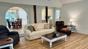 A spacious living room with a wooden floor, a beige sofa, a black leather armchair, and a coffee table with a bowl of fruit. - The Star Point Lakehouse · 3BR/2BA Retreat in Brandon (Brandon)