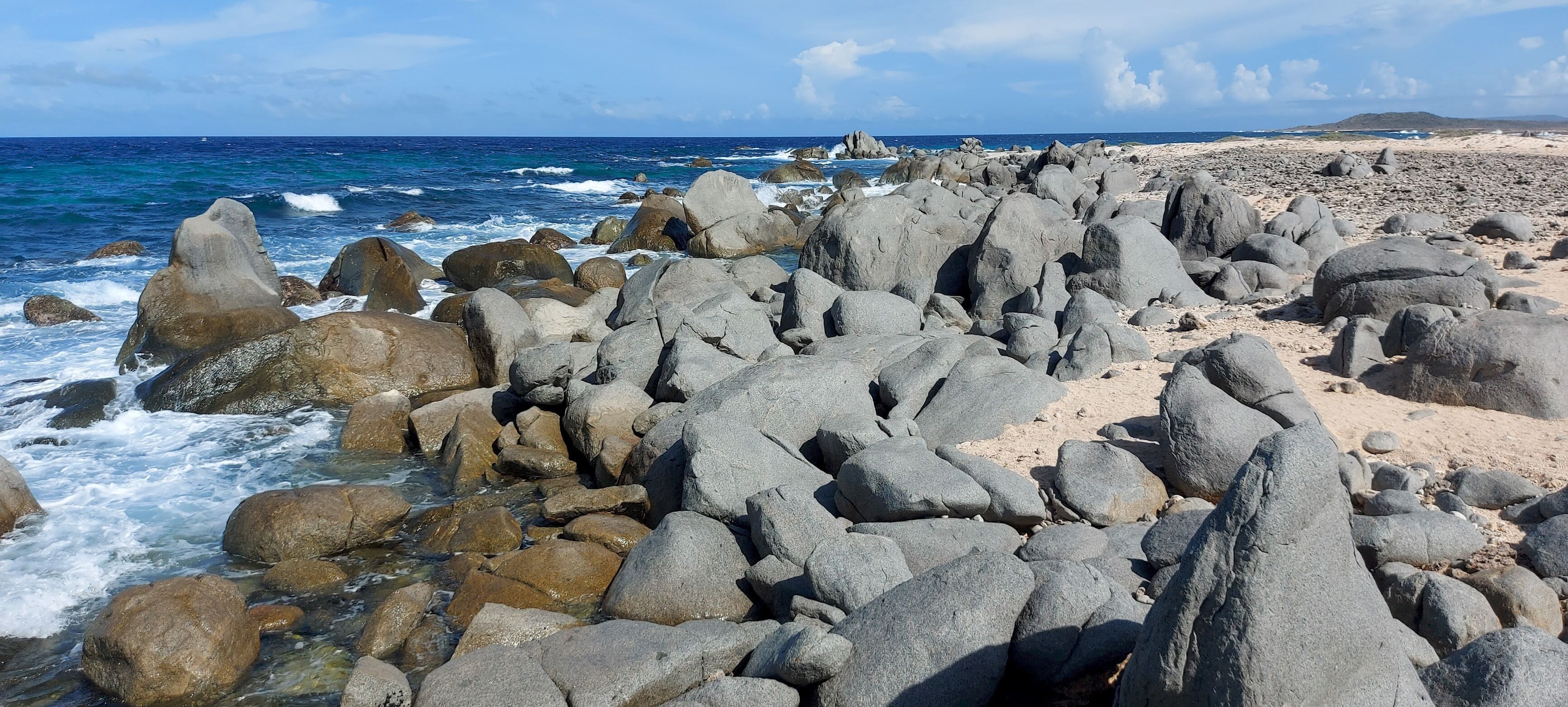 A rocky beach with large boulders and waves crashing against them.