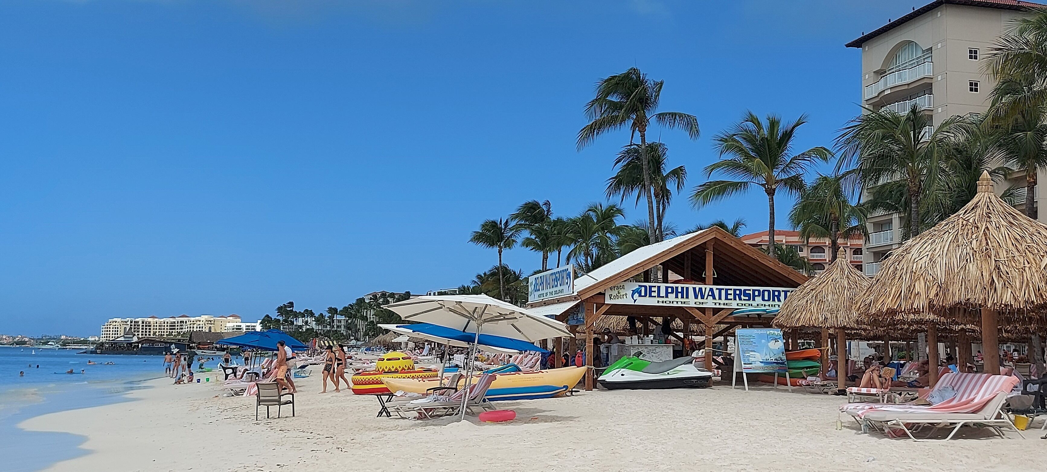 A beach with sun loungers, umbrellas, and a watersports rental area.