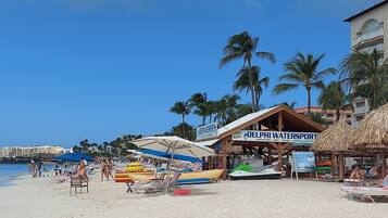 A beach with sun loungers, umbrellas, and a watersports rental area.