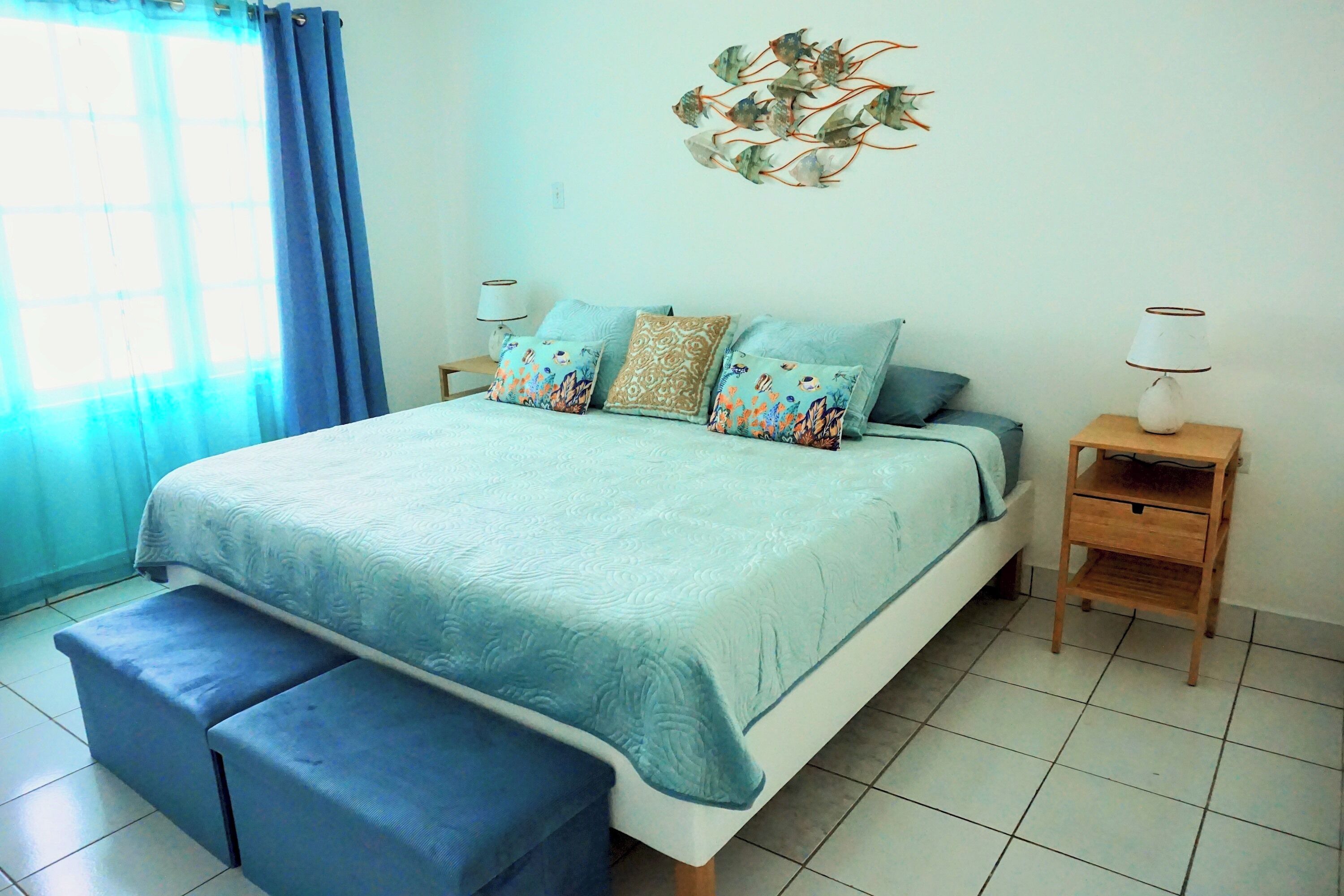 A bedroom with a bed, two bedside tables, a bench, and a wall decoration.