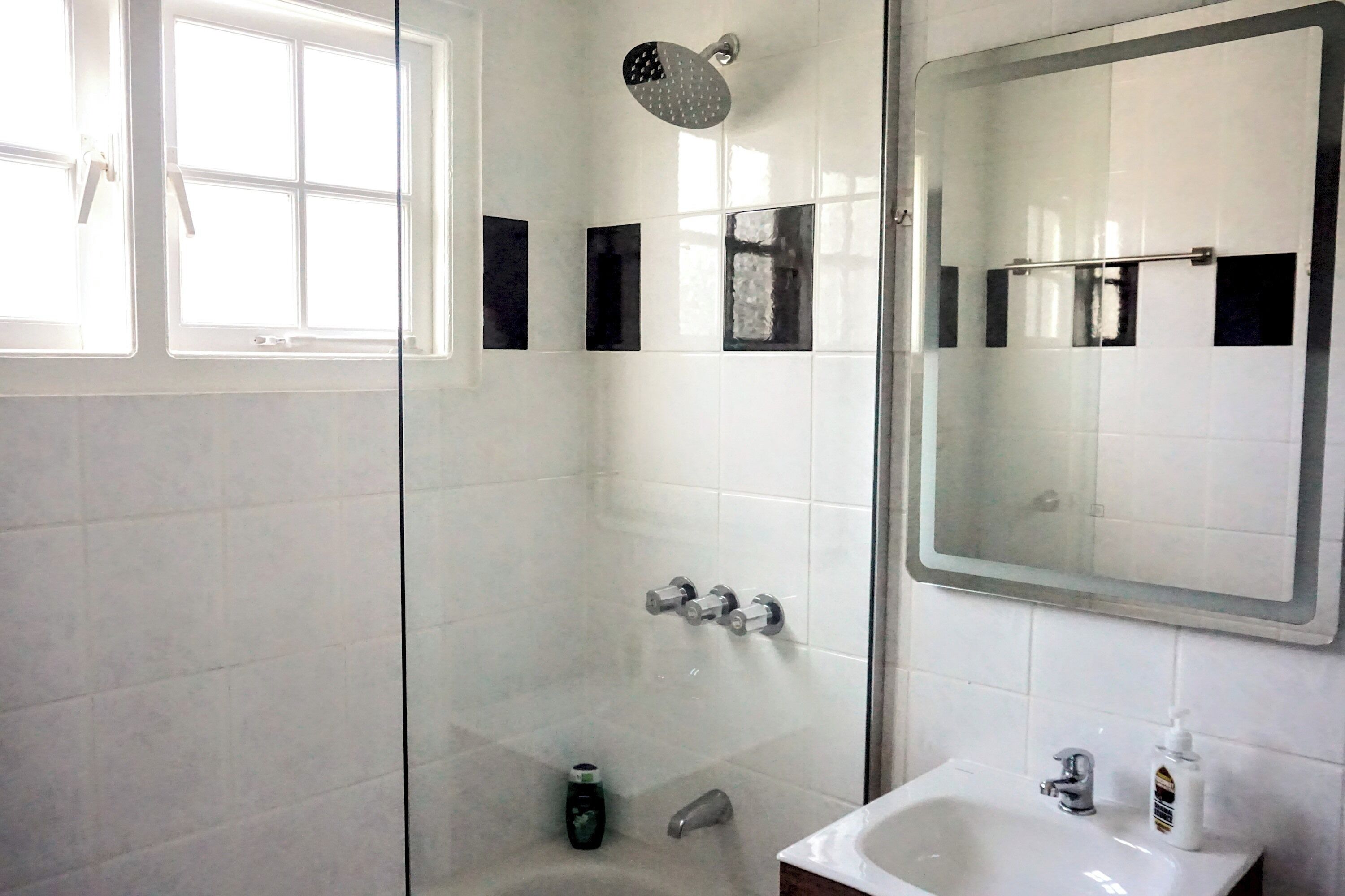 A modern bathroom with a glass-enclosed shower, a white sink, and a large mirror.