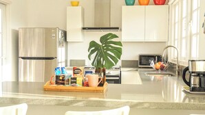 Une cuisine moderne équipée d’un réfrigérateur en acier inoxydable, d’un four à micro-ondes et d’une machine à café. On peut voir un plateau en bois contenant des aliments et une plante en pot sur le comptoir.