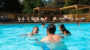 A swimming pool with people in the water and sun loungers in the background.