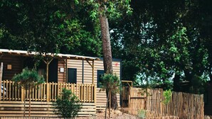 A rustic cabin with a wooden deck, surrounded by a bamboo fence and trees.