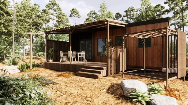 A wooden cabin with a covered patio, outdoor seating, and a view of the surrounding forest.