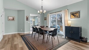 Un coin repas avec une table en bois, des chaises noires et un lustre.