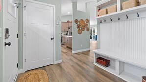 Un couloir avec une porte blanche, un plancher en bois, une étagère fixée au mur avec des paniers, et un élément décoratif mural.
