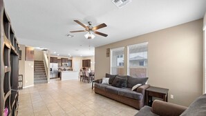 A spacious living room with a gray sofa, a coffee table, and a ceiling fan. A staircase leads to a kitchen area with modern appliances. - Spacious 4-bedroom house in charming Jarrell with AC (Jarrell)