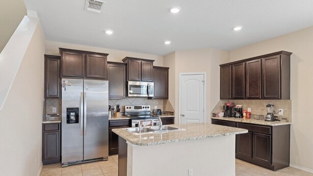 A modern kitchen with a central island, stainless steel appliances, and dark cabinetry. - Spacious 4-bedroom house in charming Jarrell with AC (Jarrell)