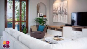 A modern living room with a white sofa, a brown armchair, a TV, and a cityscape painting. - Elegant apartment for 6 people. Private elevator and large terrace. Milan. (Milano)