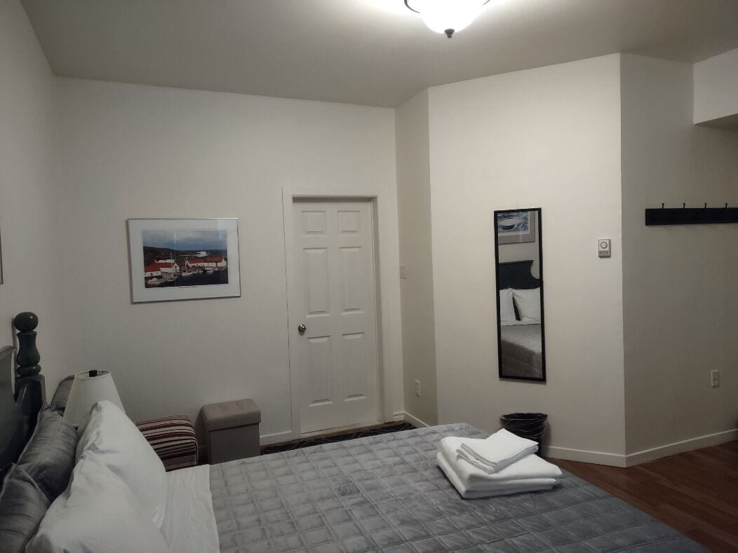 Une chambre à coucher avec un lit, une porte, un tableau encadré au mur et une petite table avec une lampe.