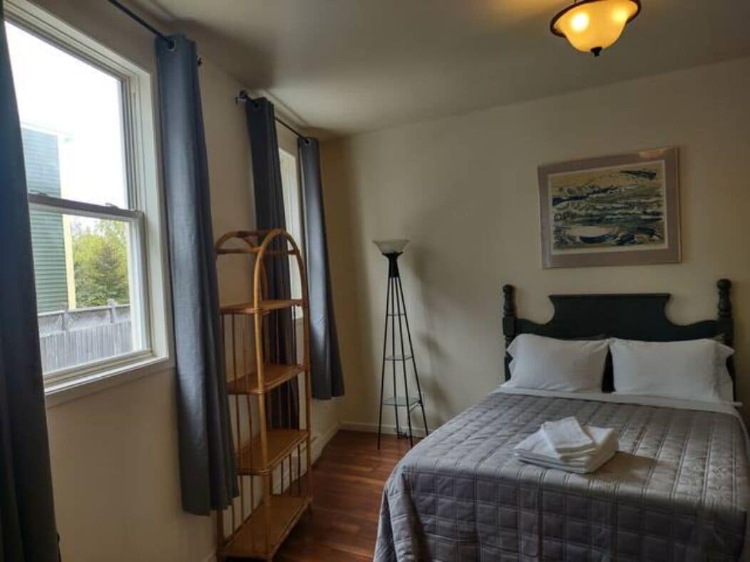 A bedroom with a bed, a painting on the wall, a window with curtains, and a wooden ladder.