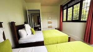 Et hotelværelse med to senge, et spejl, et vindue med gardiner og en hylde med håndklæder.