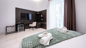 Une chambre d’hôtel moderne équipée d’un téléviseur à écran plat fixé au mur, d’un bureau, d’une chaise et d’un lit recouvert d’une couverture à motifs verts.