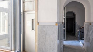 Un couloir doté d’un sol en marbre, d’une porte en verre et d’une porte en arc donnant accès à une autre pièce.