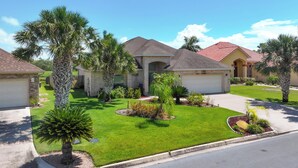A residential area with houses featuring brick exteriors, red-tiled roofs, and well-maintained lawns with palm trees. - Poolside Bliss/fenced yard/water views/golf/pickleball/pets/tennis/sun & fun (Laguna Vista)