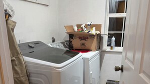 Une buanderie équipée d’un lave-linge, d’un sèche-linge et d’un carton contenant des produits de nettoyage.