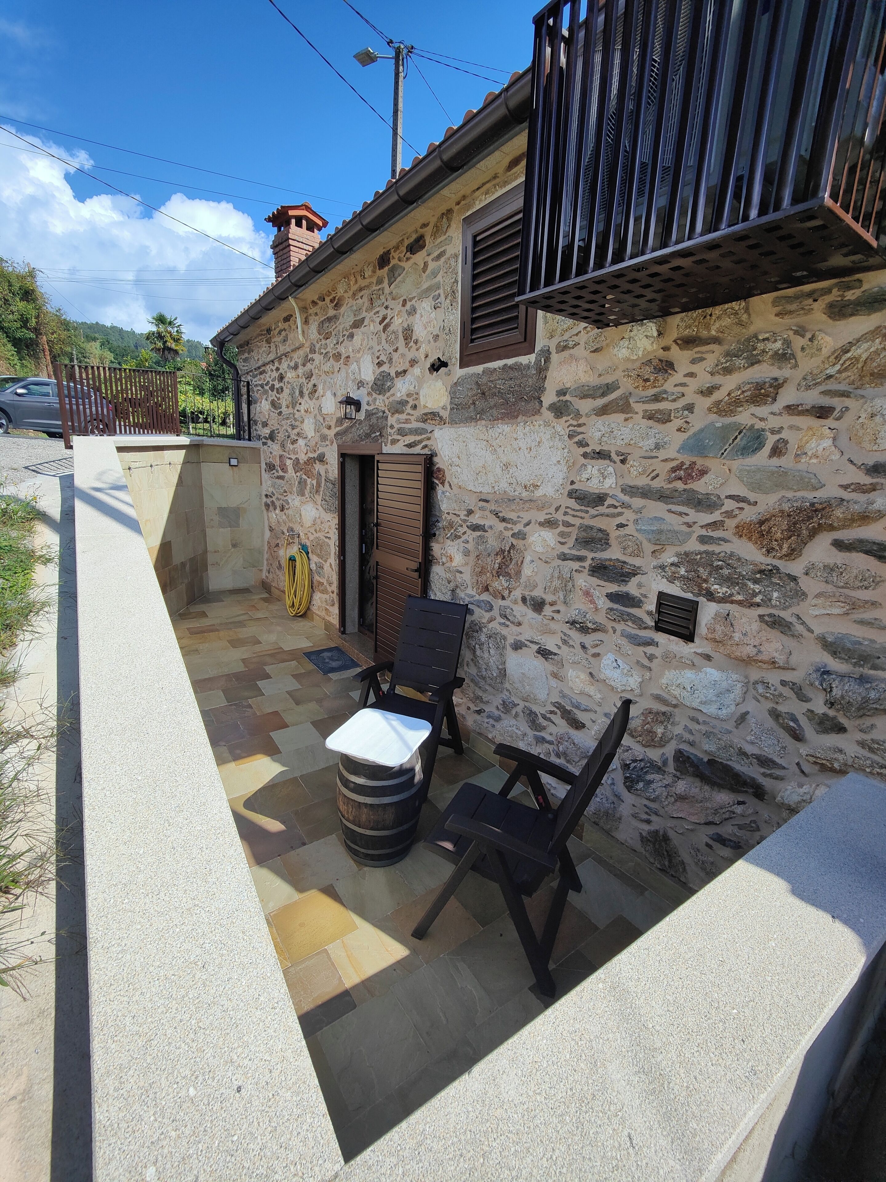 Un edificio de piedra con un patio que incluye un banco de piedra, una mesita y un barril.