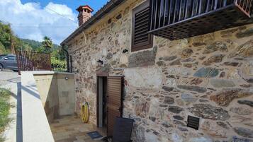 Un edificio de piedra con un patio que incluye un banco de piedra, una mesita y un barril.