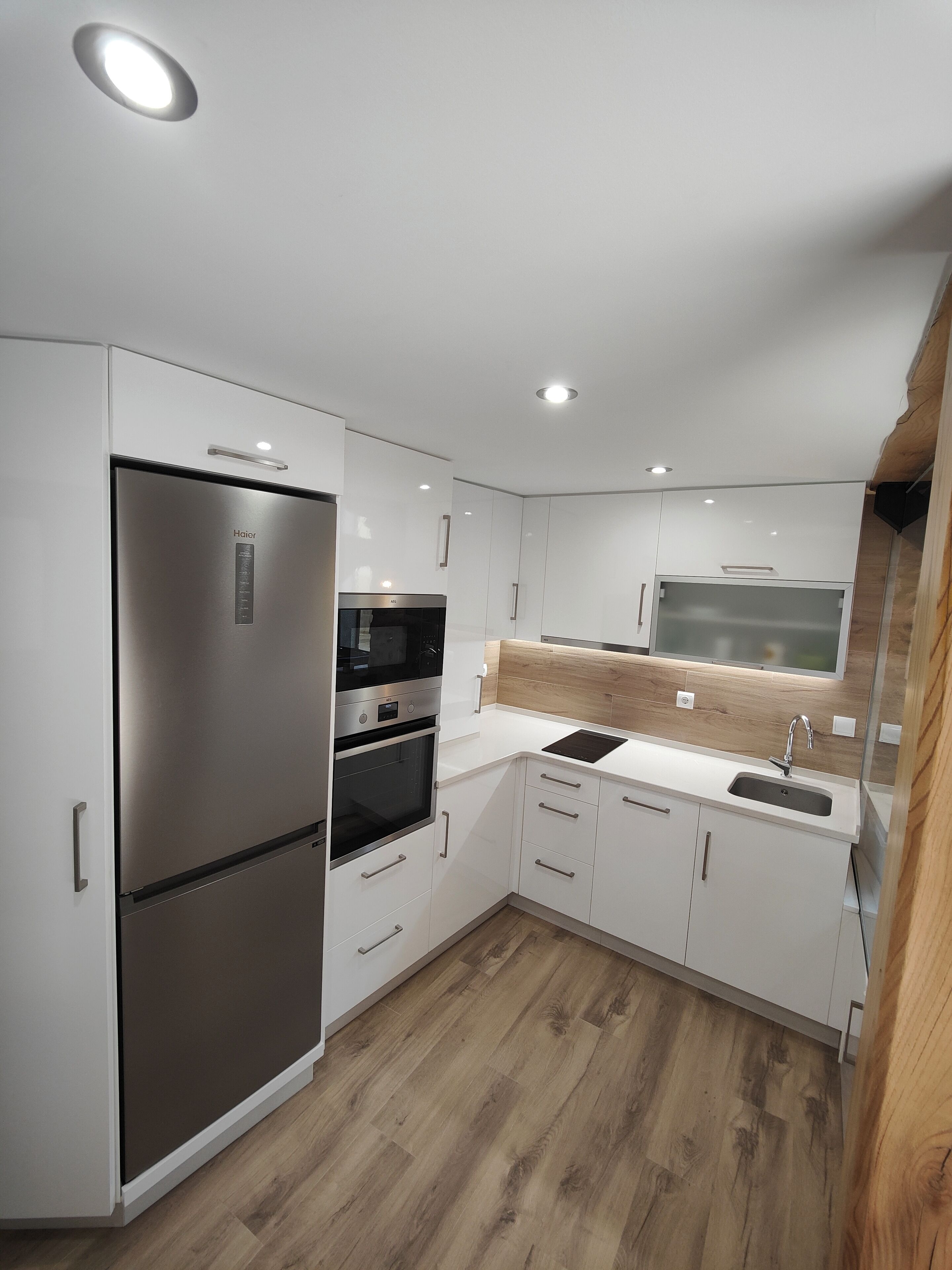Een moderne keuken met witte kastjes, roestvrijstalen apparatuur en een houten vloer.