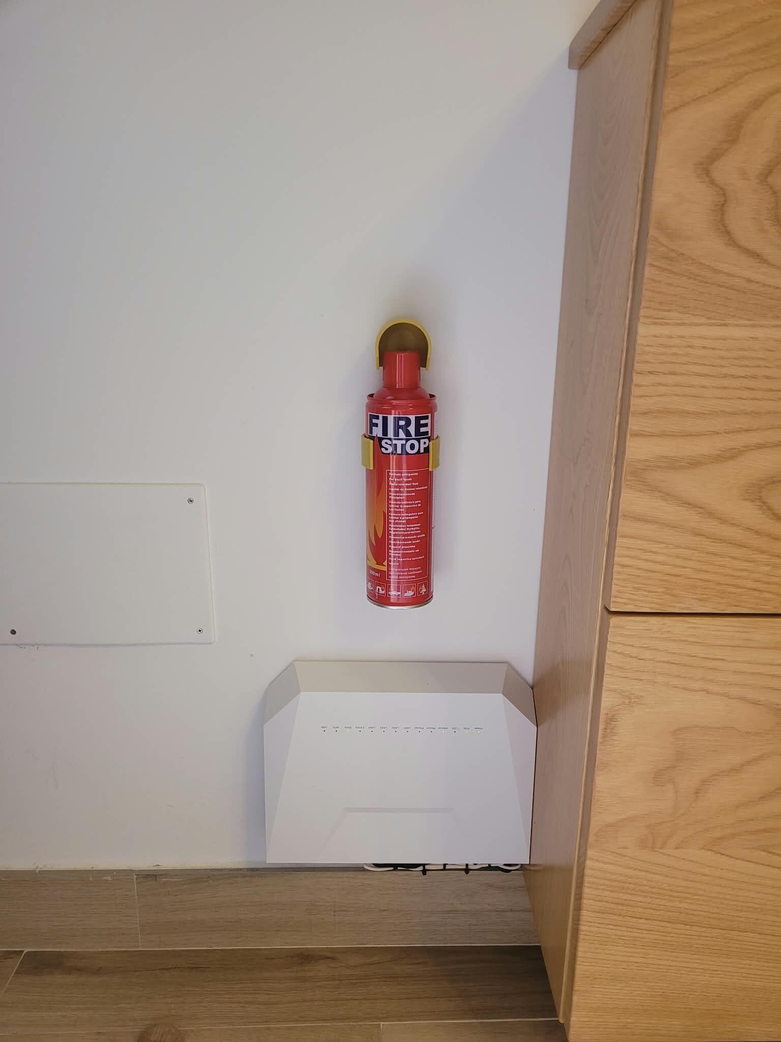 Extintor de incendios sujeto a una pared blanca en una habitación con suelo de madera y un armario blanco.