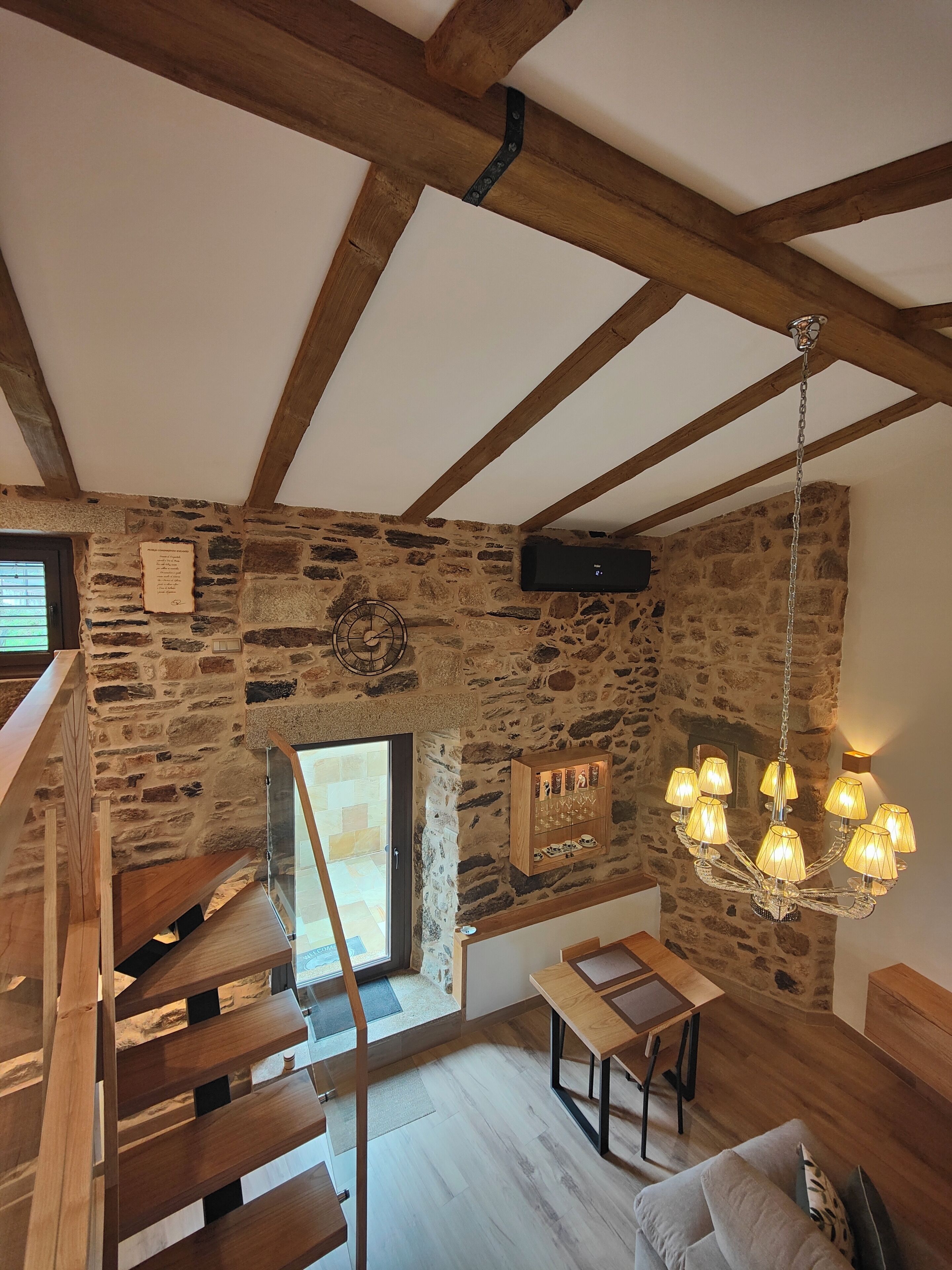 Un intérieur rustique avec des poutres apparentes, un mur en pierre, un lustre et un escalier.