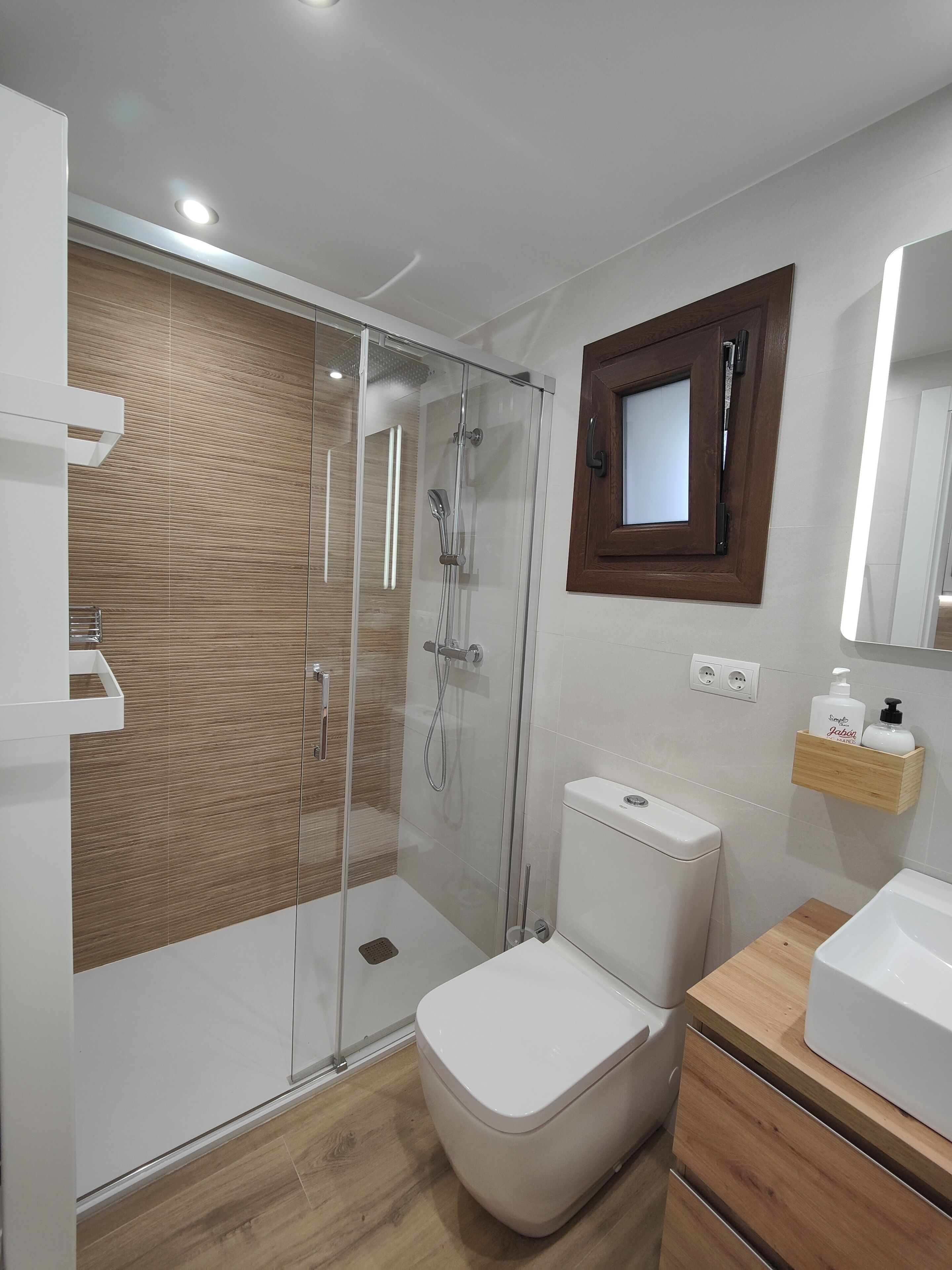 A modern bathroom with a glass-enclosed shower, a white toilet, and a wooden vanity with a mirror.