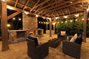 An outdoor patio with a stone fireplace, wicker furniture, and string lights. - Harpers Ferry: Hot Tub • Patio • Fireplace (Harpers Ferry)