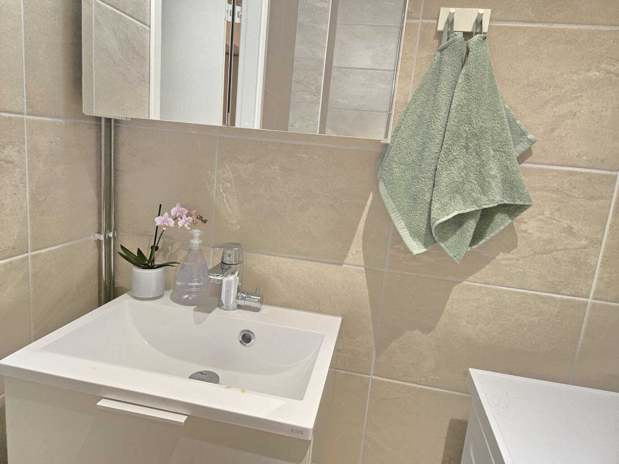 Un baño con un lavabo blanco, un espejo encima y una toalla colgada en un perchero.