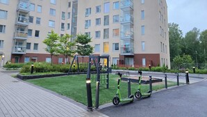 A modern apartment building with multiple balconies, a small park area with a playground, and electric scooters parked in front. - Viherpihan helmi | Free parking & Netflix | 5G | 100 m to metro (Espoo)