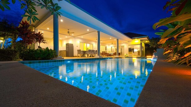 A modern hotel with a swimming pool, outdoor seating, and a well-lit interior. - TropicalFamilyVilla w Pool&Garden ML103 (Hua Hin)