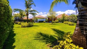 A well-maintained garden with palm trees, a lawn, and a building with a red roof. - TropicalFamilyVilla w Pool&Garden ML103 (Hua Hin)