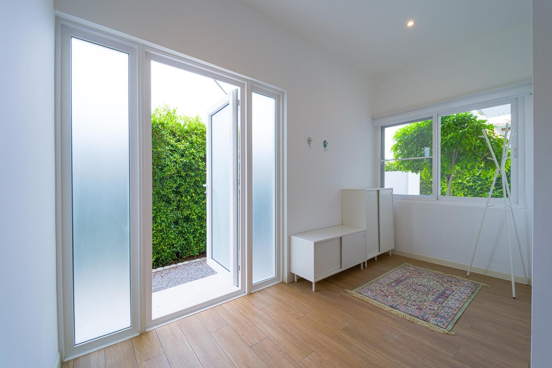 A spacious room with large sliding glass doors, a white bench, a patterned rug, and a ladder leaning against the wall.