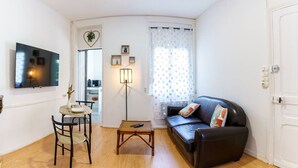 A living room with a black leather sofa, a wooden coffee table, a TV mounted on the wall, and a dining area with a small table and chairs. - Le Spacieux, Gare et Centre, Fibre et Bureau, Idéal Pro (Saint-Quentin)