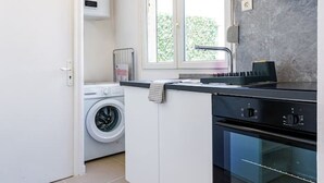 A compact kitchen with a washing machine, a stove, and a window providing natural light. - Le Spacieux, Gare et Centre, Fibre et Bureau, Idéal Pro (Saint-Quentin)