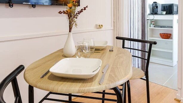A dining area with a table set for two, a vase with flowers, and a television mounted on the wall. - Le Spacieux, Gare et Centre, Fibre et Bureau, Idéal Pro (Saint-Quentin)