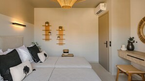 Une chambre moderne avec deux lits, une étagère murale agrémentée de plantes, un luminaire suspendu en fibres naturelles et un banc en bois.