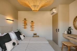 A modern bedroom with two beds, a wall-mounted shelf with plants, a woven ceiling light, and a wooden bench. - Assos Reverie Villa (9GGR+RXG Erisos, Greece)