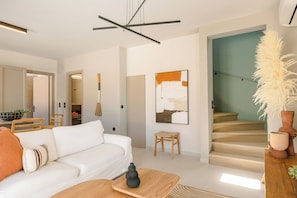 A modern living room with a white sofa, a wooden coffee table, and a staircase leading to an upper floor. - Assos Reverie Villa (9GGR+RXG Erisos, Greece)