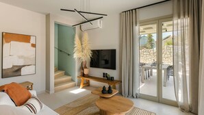 Un salon moderne comprenant un canapé, une table basse, un téléviseur, un escalier et donnant sur une terrasse extérieure.