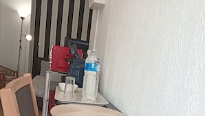 A room with a bed, a bedside table with a lamp, a water bottle, and a red suitcase. - Cosy Vallée Studio (Pau)